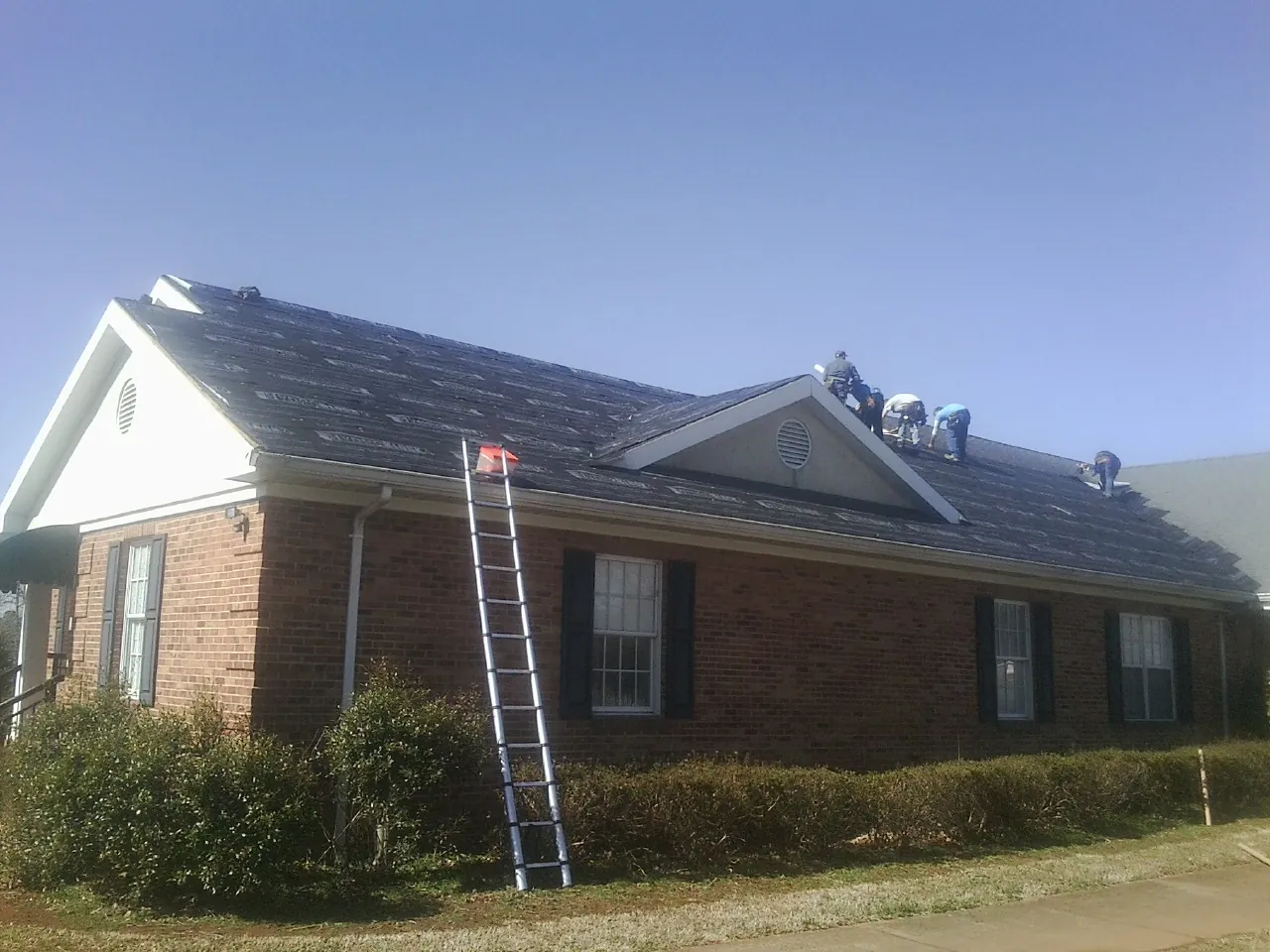Crew tearing shingles off a brick ranch roof with a ladder set — Metal Roof Repair work by our crew in Olivebridge