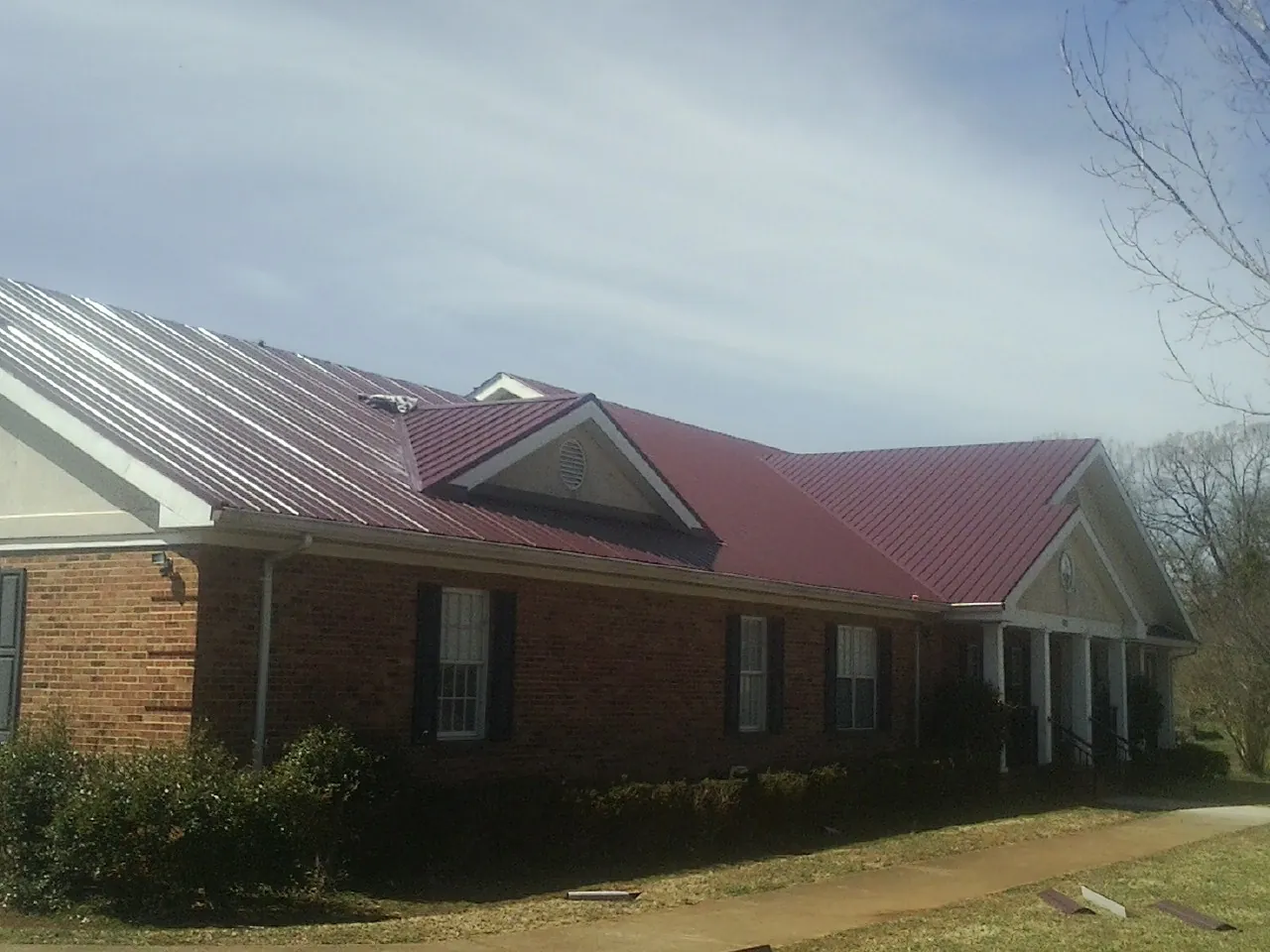 Red metal roof with gabled entries on a long brick building, from a Hail Damage Roof Repair job in Olivebridge