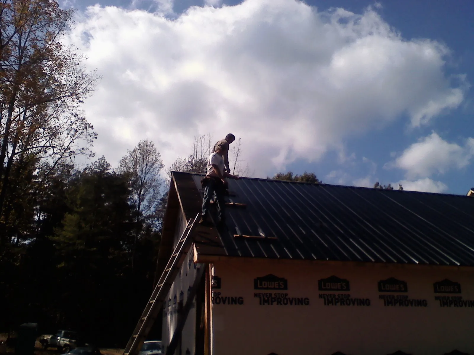 Roofer fastening dark metal panels high against a cloudy sky, from a Roof Inspection job in Olivebridge