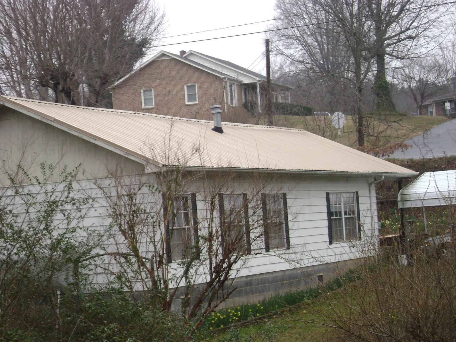 Tan metal roof on a white sided house set into a hillside — Commercial Roofing by Roofing Brothers in Olivebridge
